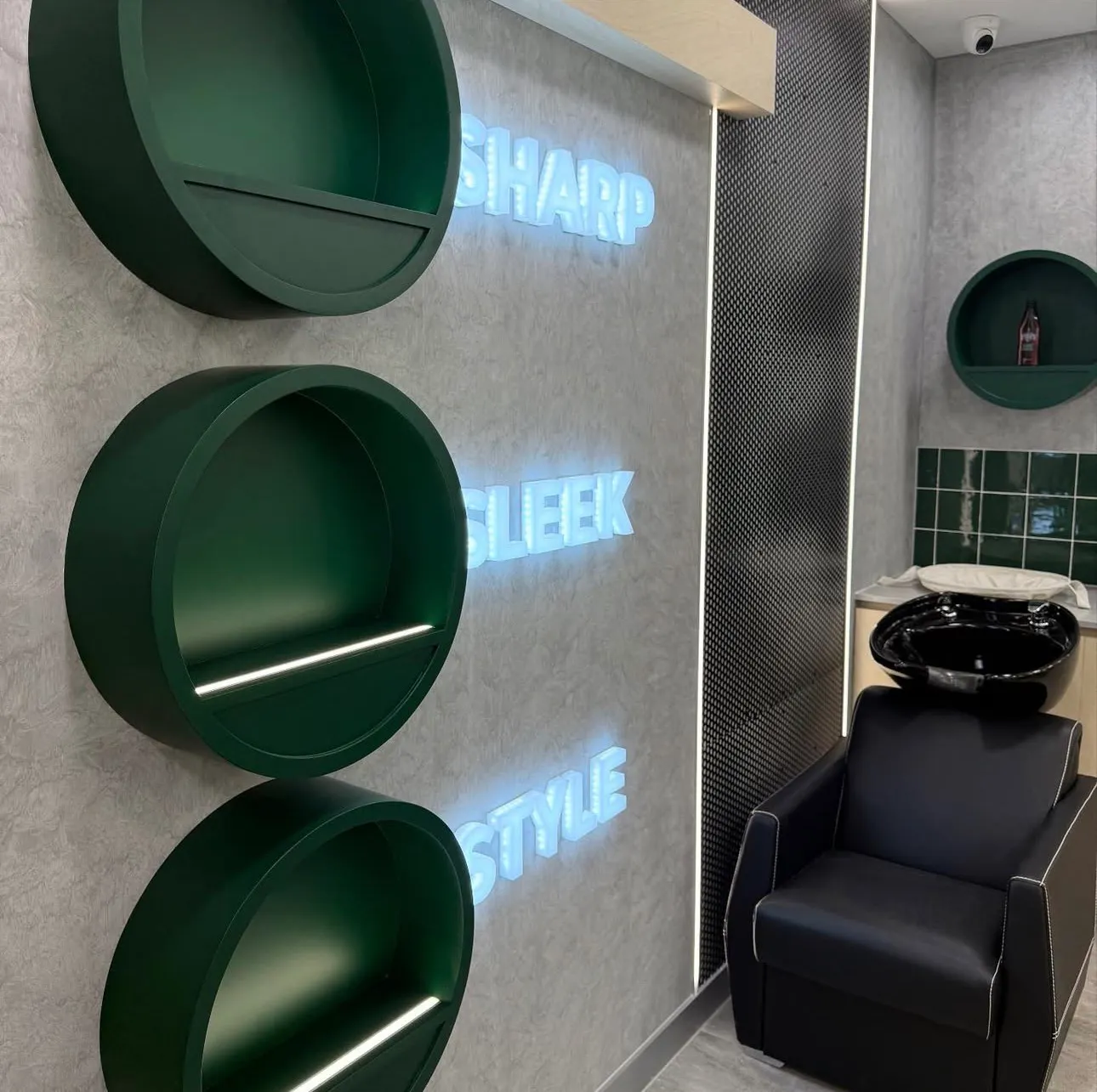Concrete-look feature wall with illuminated neon text, green circular shelves, and a wash basin.