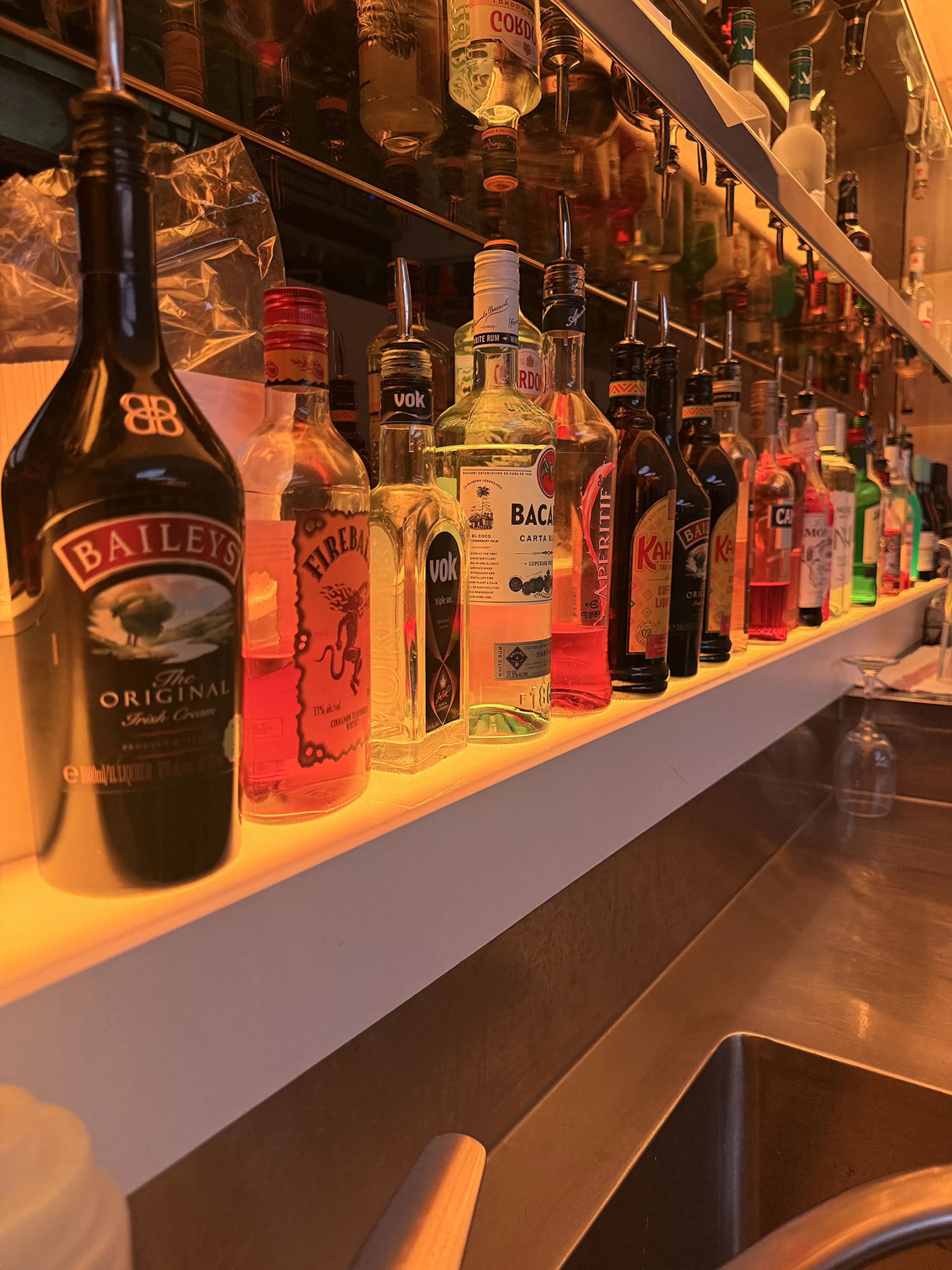 Close-up of bar shelf display with under-counter warm LED strip lighting illuminating liquor bottles