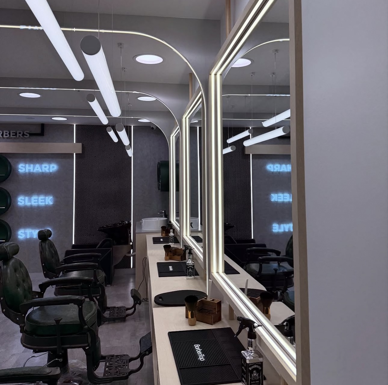 Row of barber vanity stations showing backlit mirrors and suspended cylindrical lights.