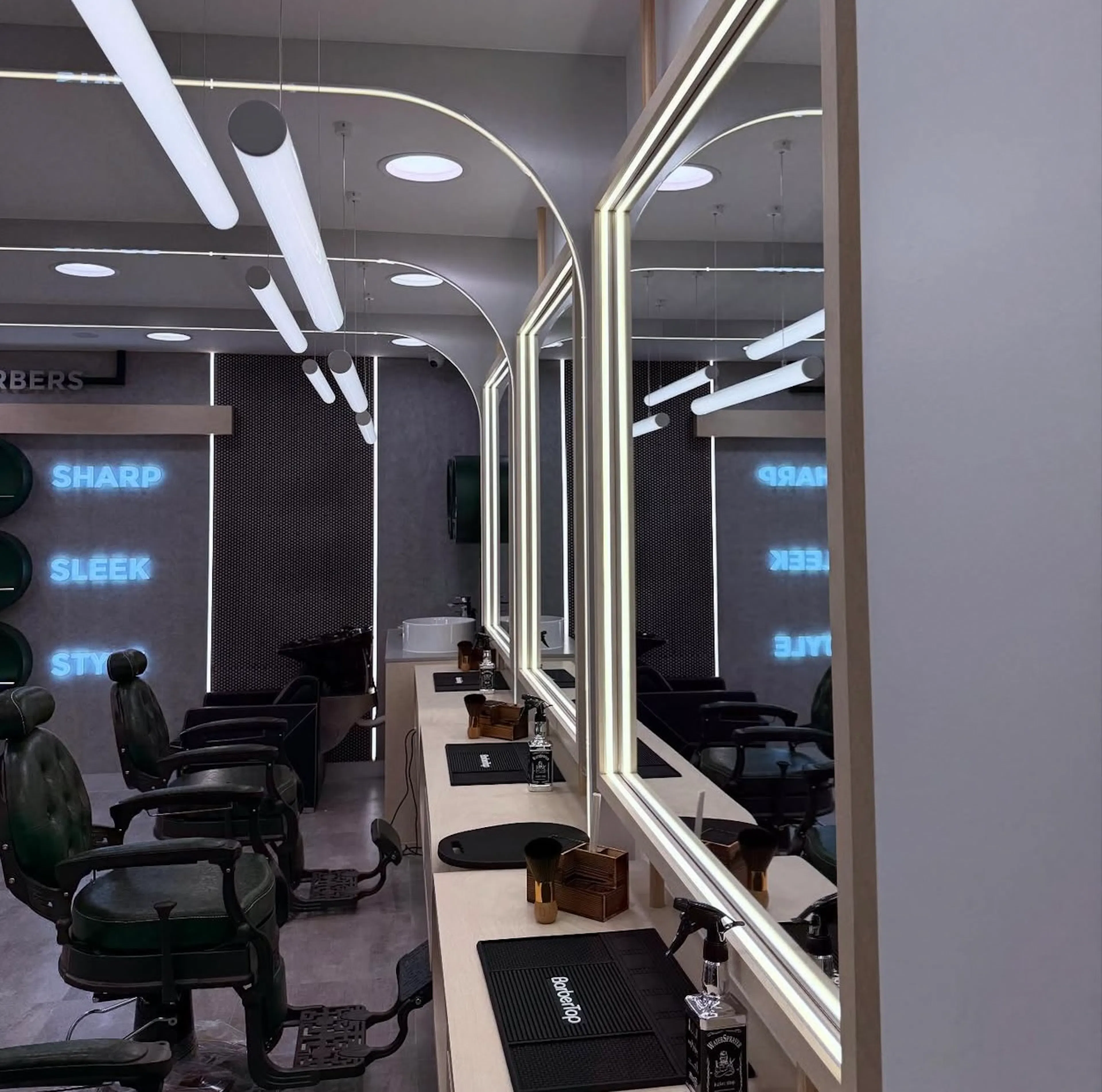 Row of barber vanity stations showing backlit mirrors and suspended cylindrical lights.