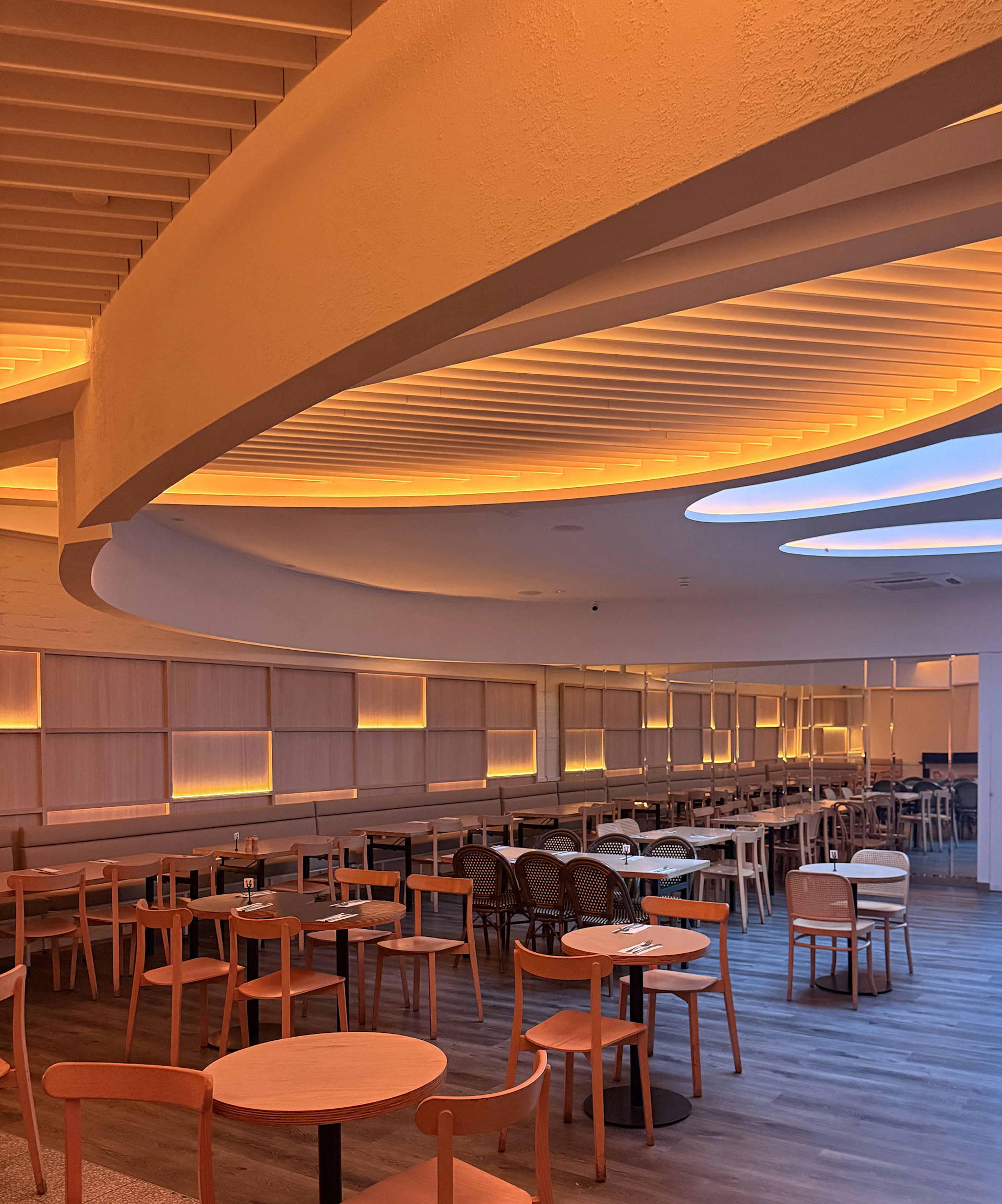 Full dining area overview showing custom architectural ceiling illumination, back-lit wall panels, and seating layout