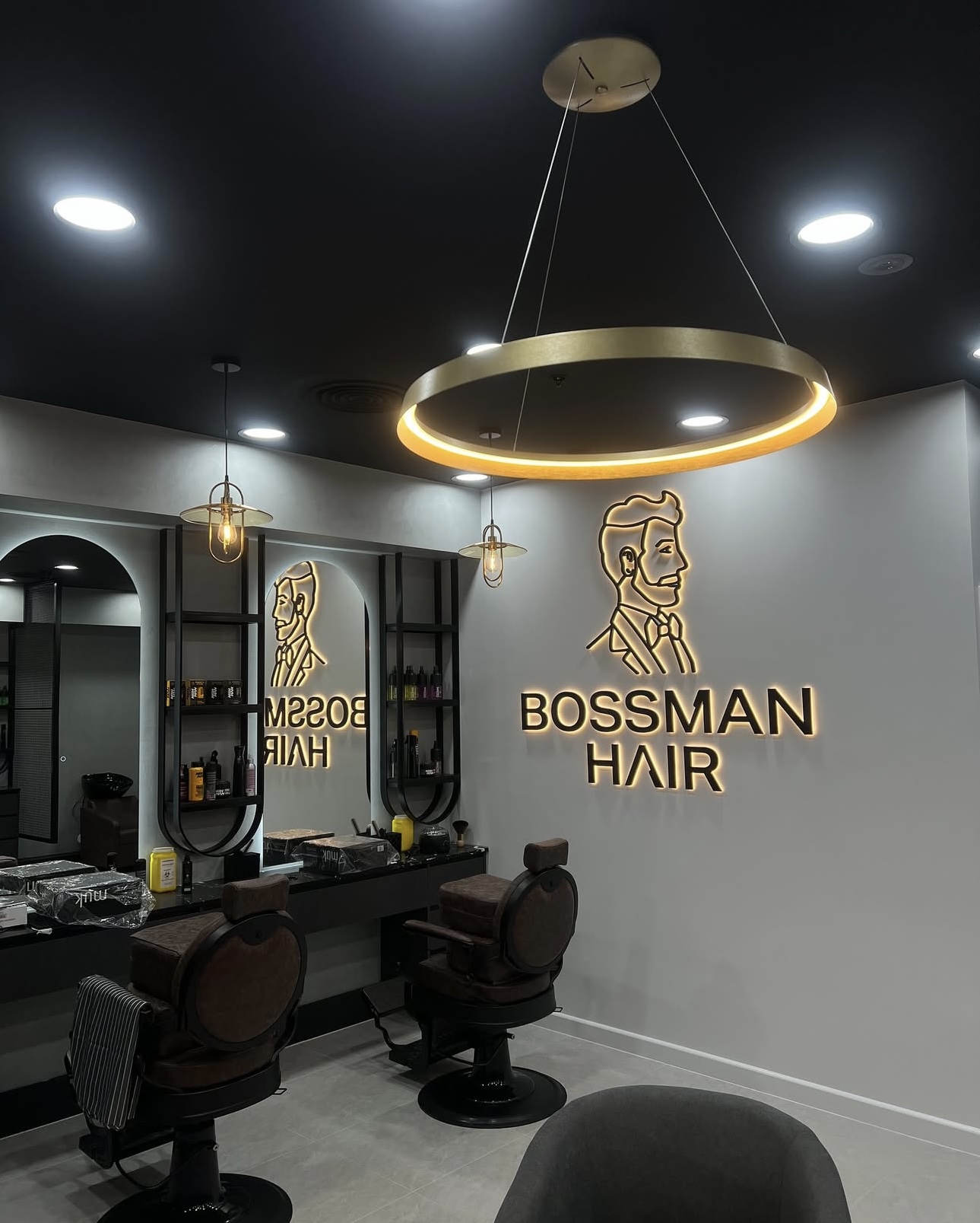 Bossman Hair interior featuring backlit logo signage, a gold ring pendant light, and leather barber chairs.