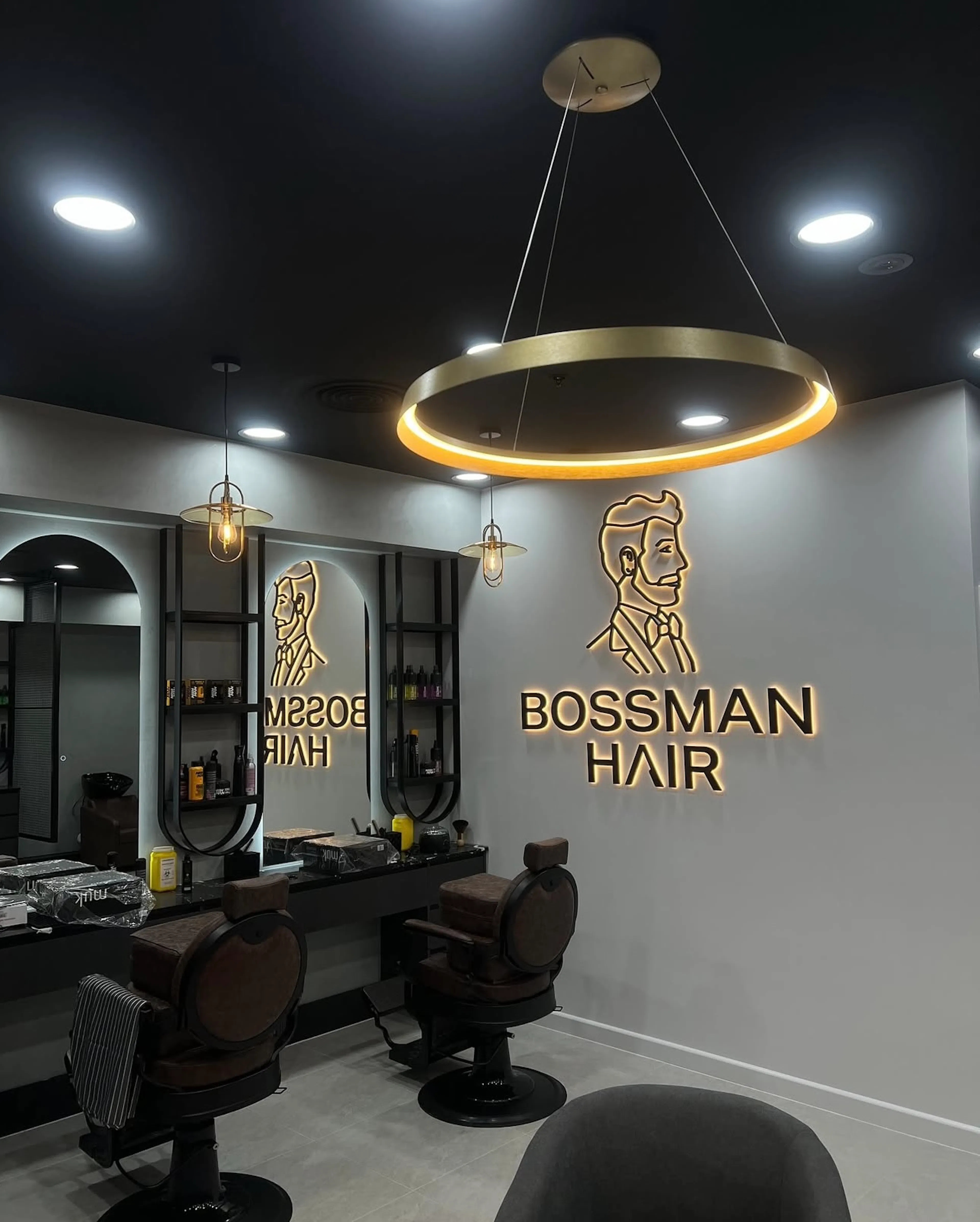 Bossman Hair interior featuring backlit logo signage, a gold ring pendant light, and leather barber chairs.