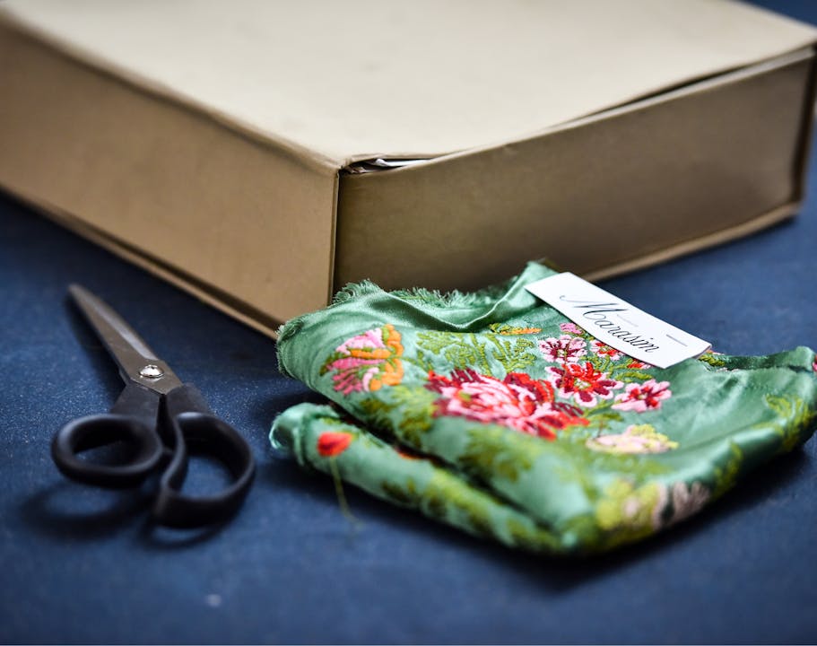 Scissors, floral fabric, and a shipping box laying next to each other