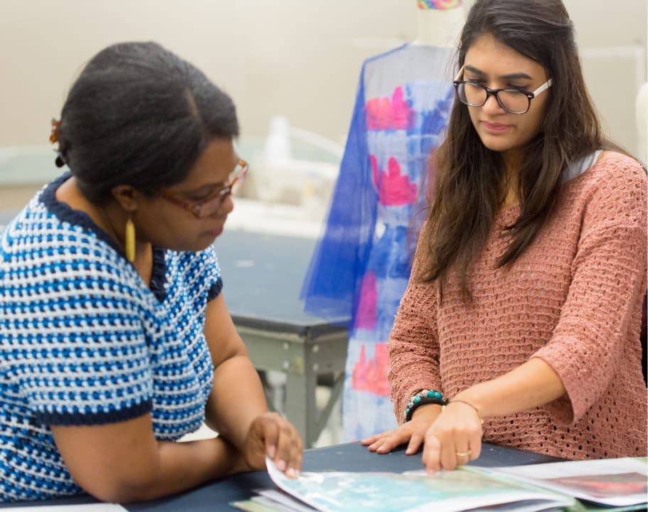 Two students looking through a fashion book as they design their own fashion pieces