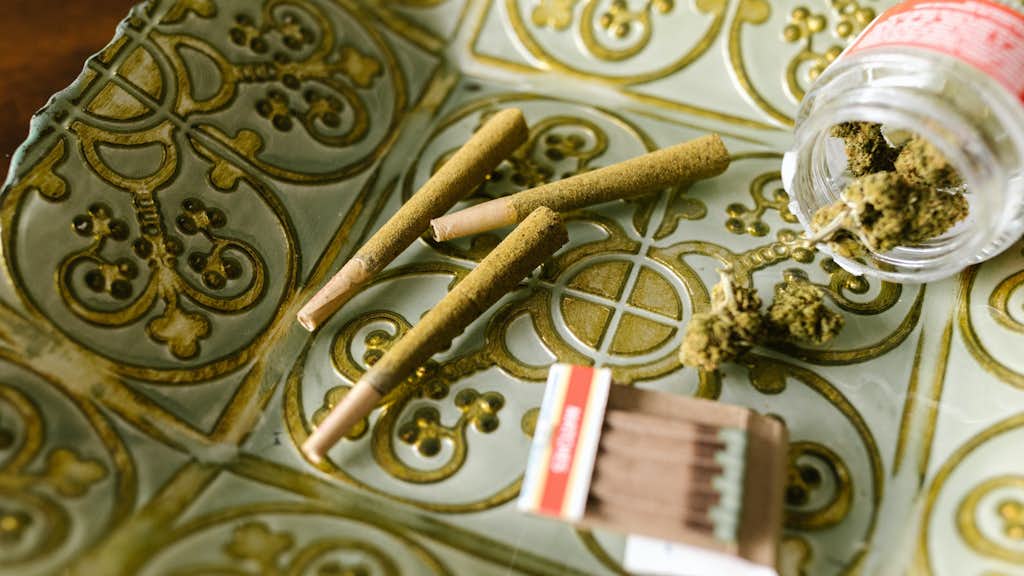 Joints, Streichhölzer und ein Glasbehälter mit Cannabis Blüten auf dem Tisch.