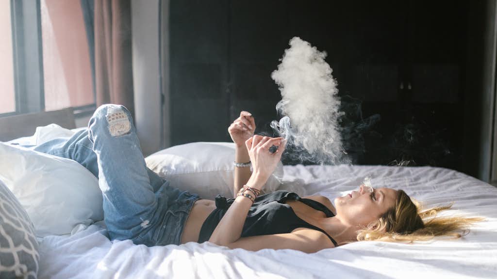 Frau liegt im Bett mit einem Joint in der Hand