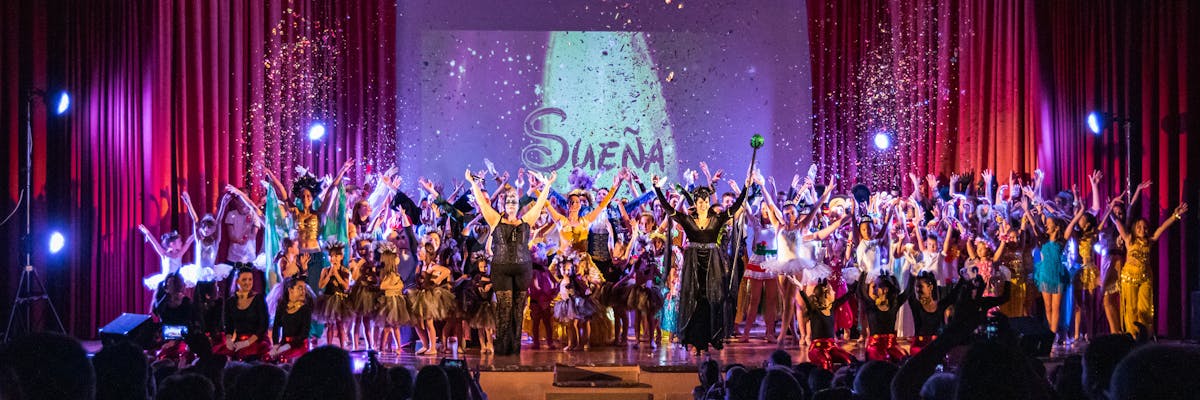 Grupo de alumnos y alumnas de una escuela de danza saludando sobre un escenario.