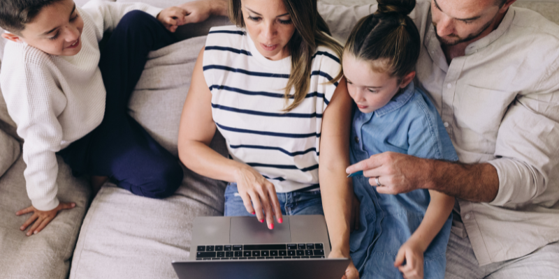 Padres e hijos en el sofá mirando la pantalla de un ordenador portátil
