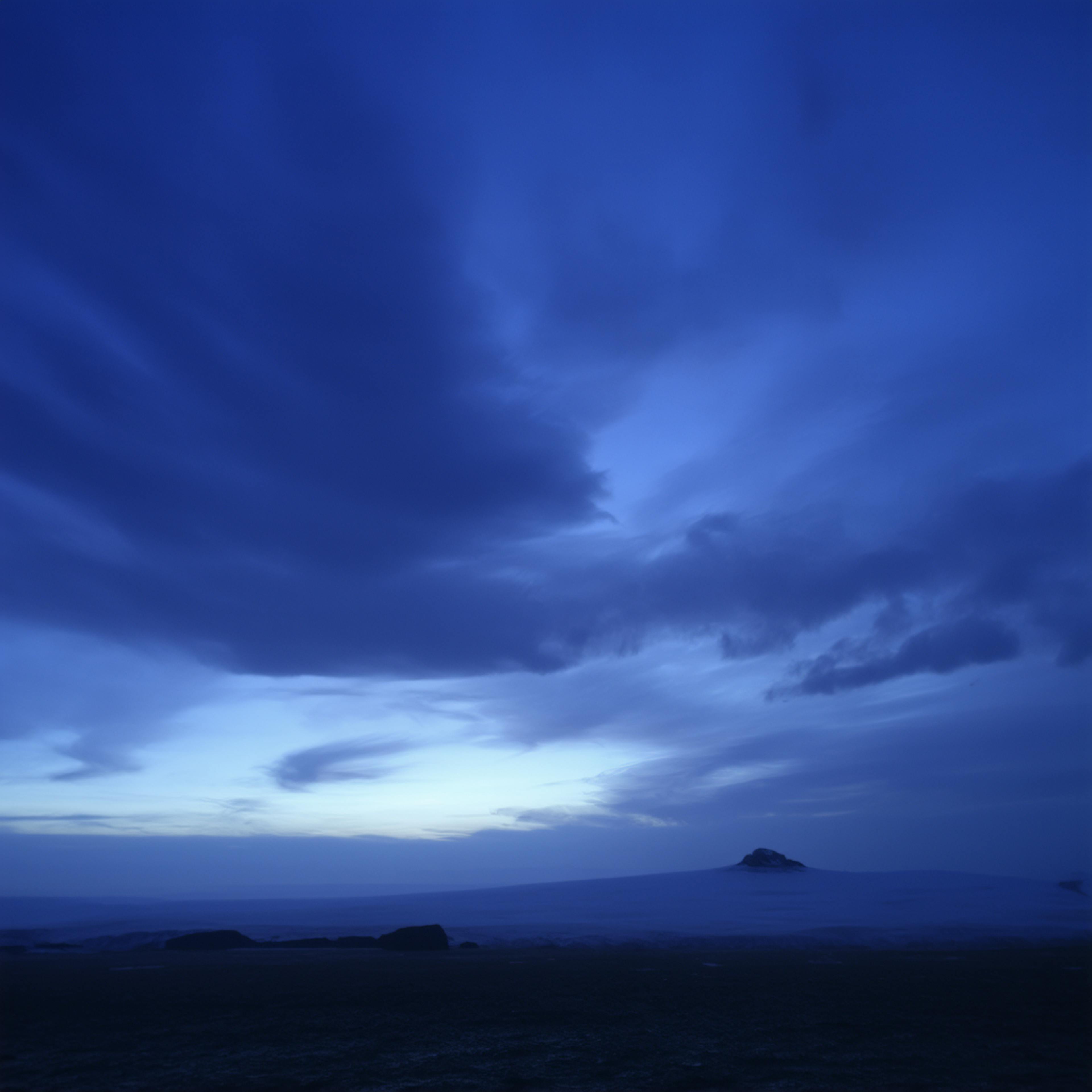 A serene blue-toned evening sky with soft clouds drifting above a distant island, showcasing the tranquility of monochromatic colors in nature.