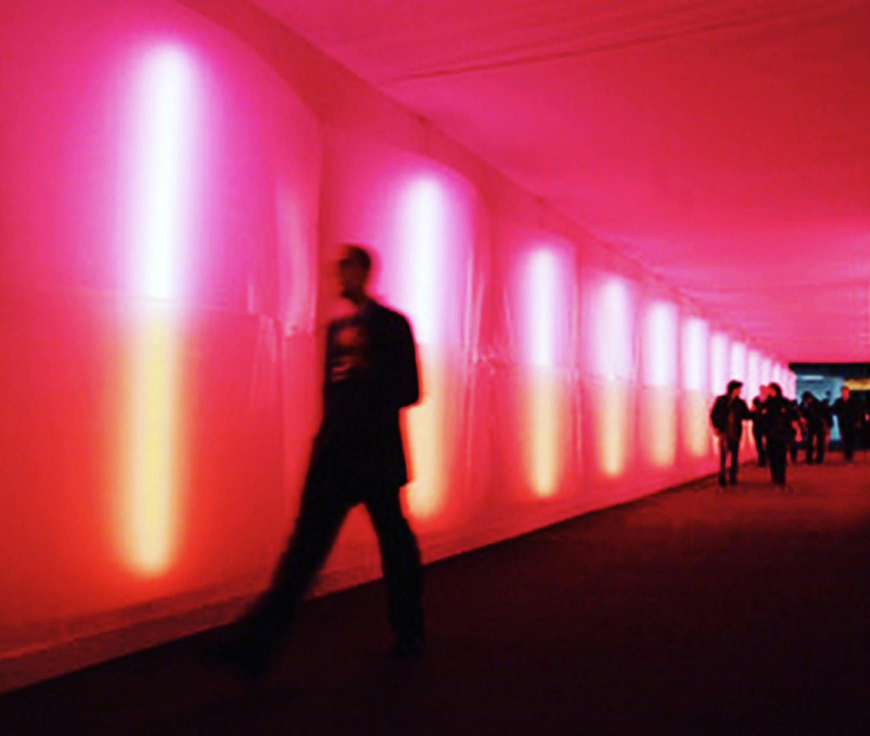 A silhouetted figure walks through a vibrant corridor illuminated by vertical neon lights, representing the dynamic and immersive environments often associated with modern sound design jobs.