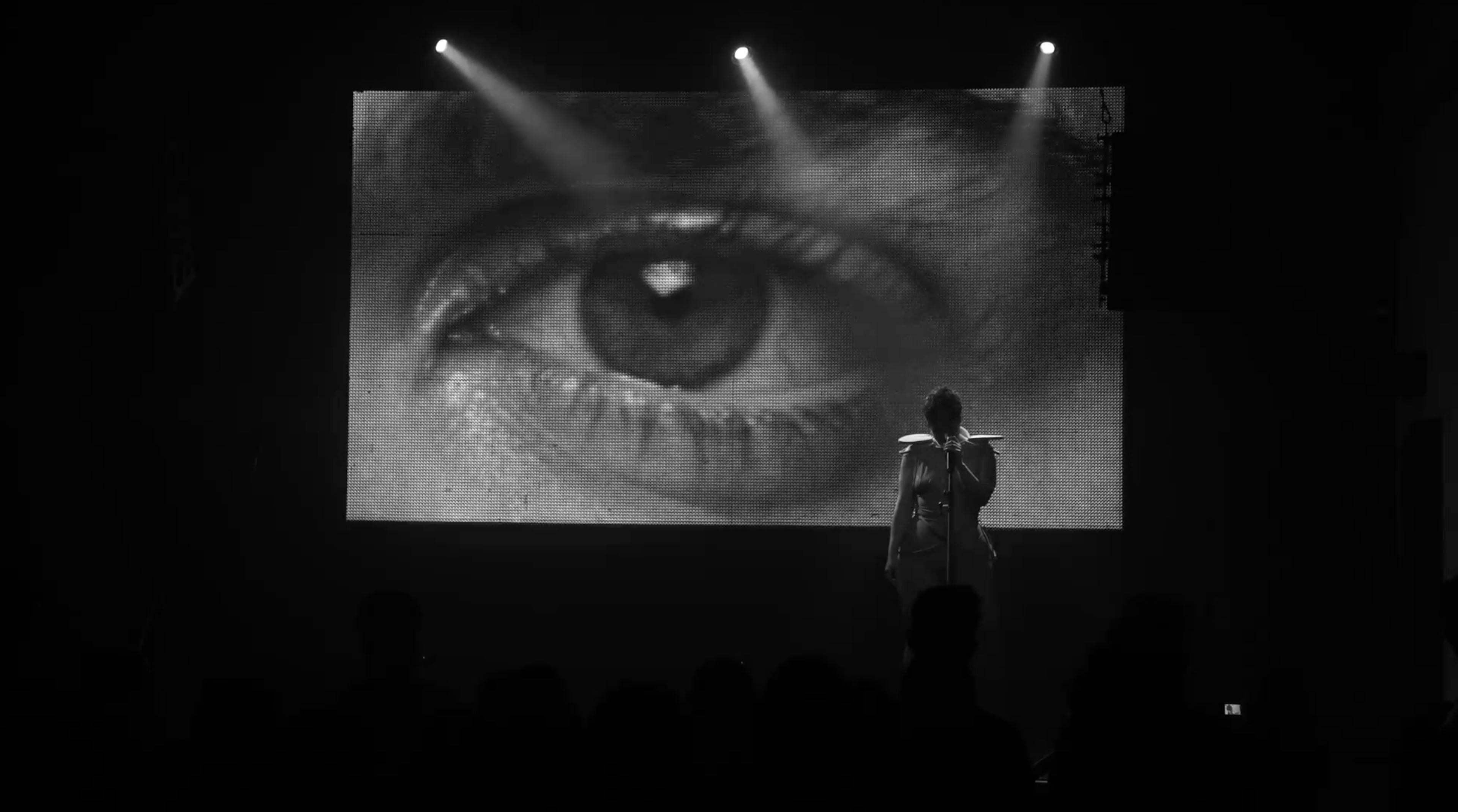 Performer in front of large projected eye