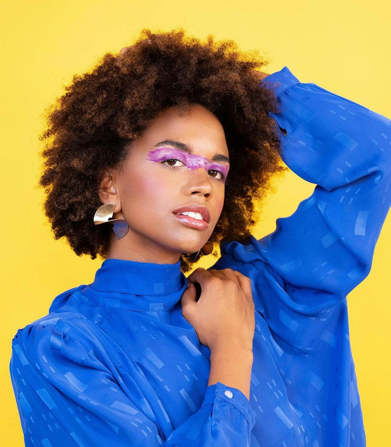 Black woman in blue shirt with futuristic eye makeup against a yellow background