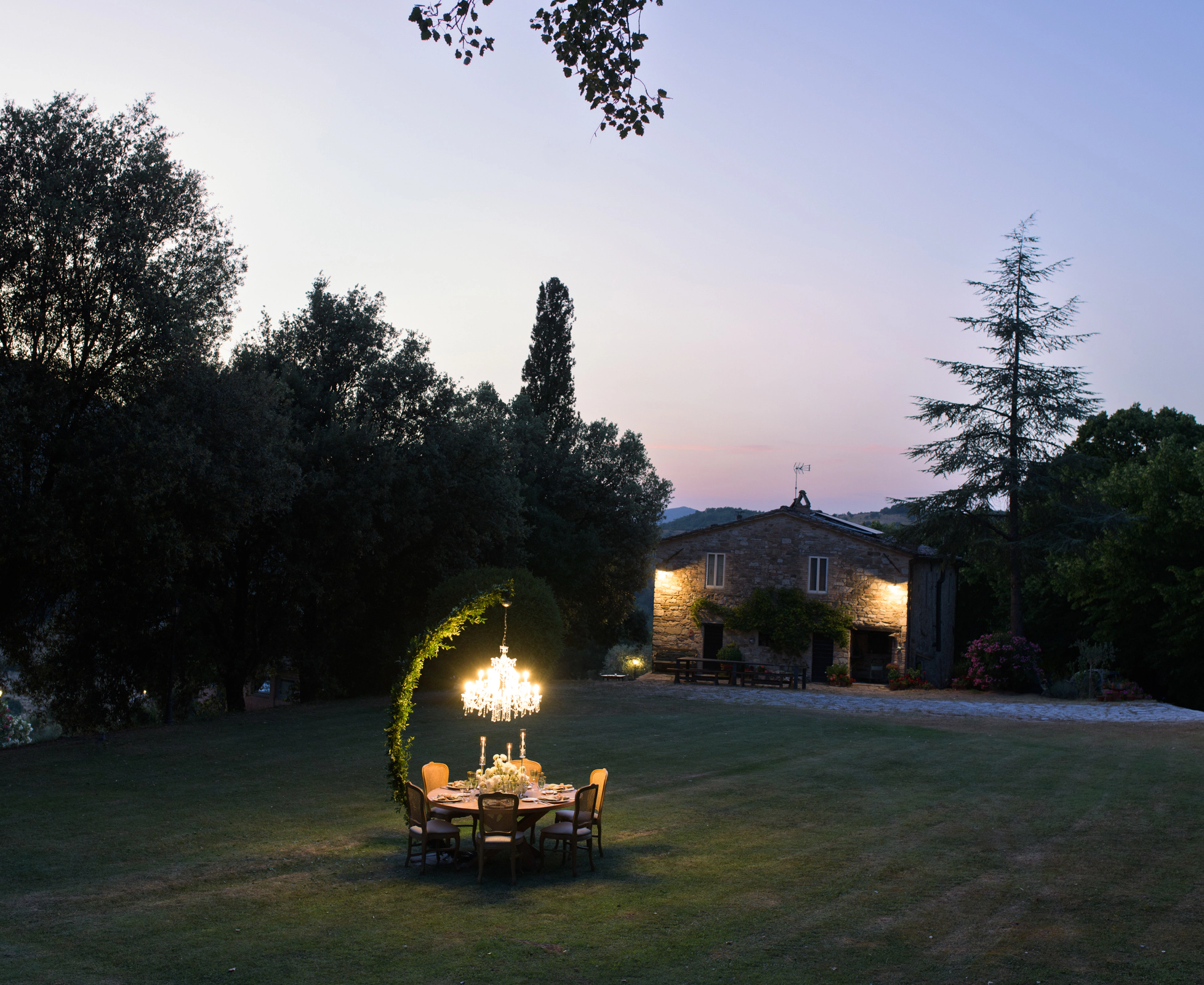 Outdoor wedding reception long table with magenta floral arrangements and gold candelabras at golden hour, with mountain and countryside backdrop at La Fonte, Italy