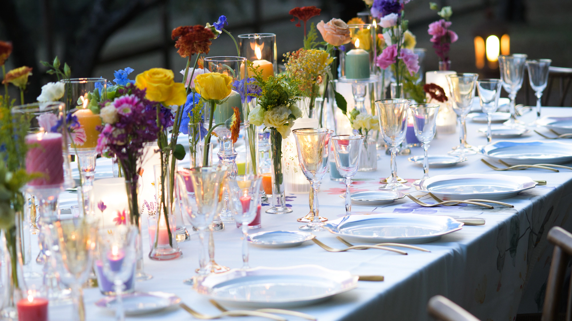Close-up of a vibrant wedding tablescape with multicolored flowers, mixed glassware, gold cutlery and candlelight at La Fonte venue, Italy