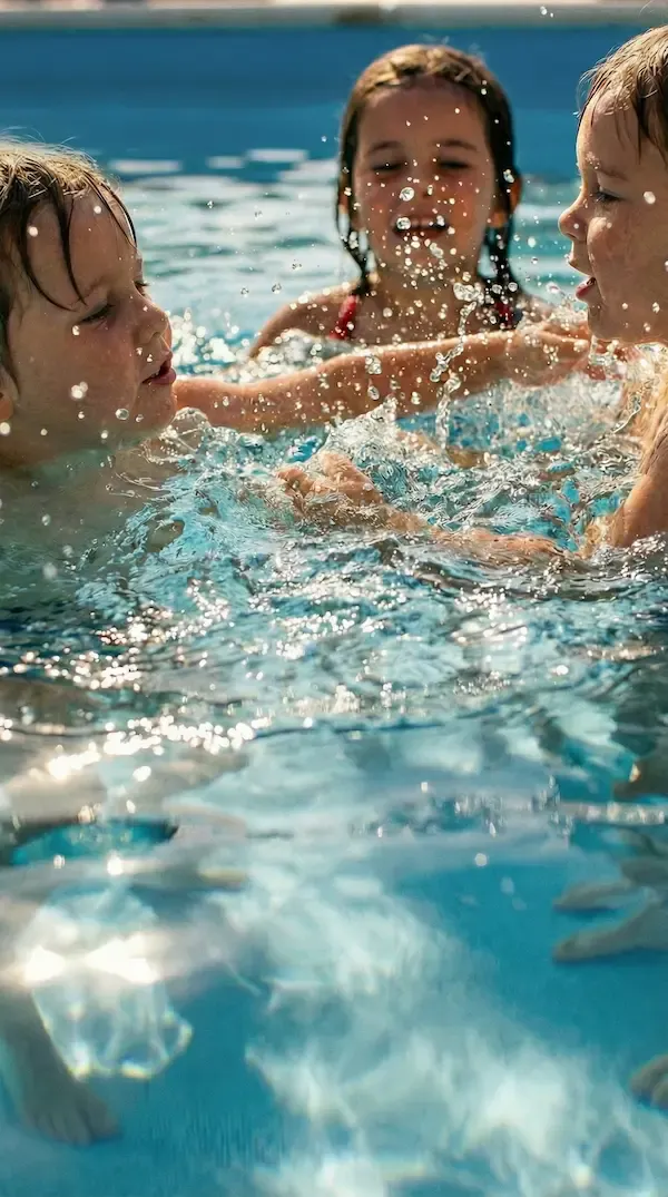 Trois enfants jouant et s'éclaboussant dans une piscine, gerbe d'eau au premier plan