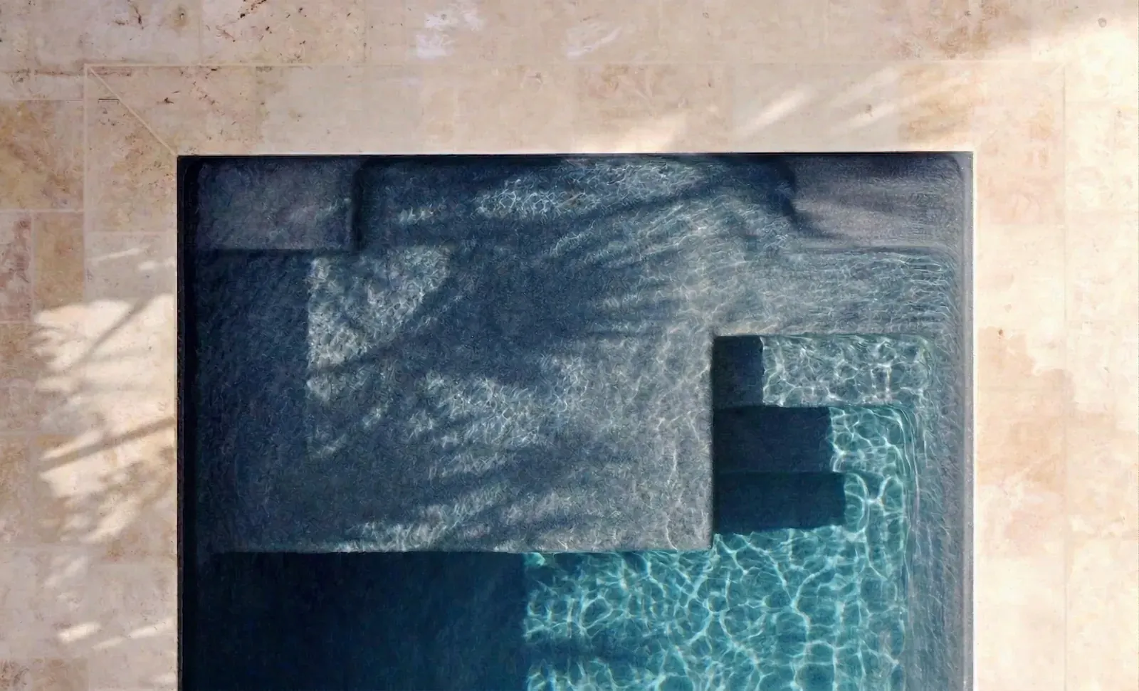 Vue aérienne d'une piscine coque à revêtement gris foncé, escalier d'angle et margelle en travertin