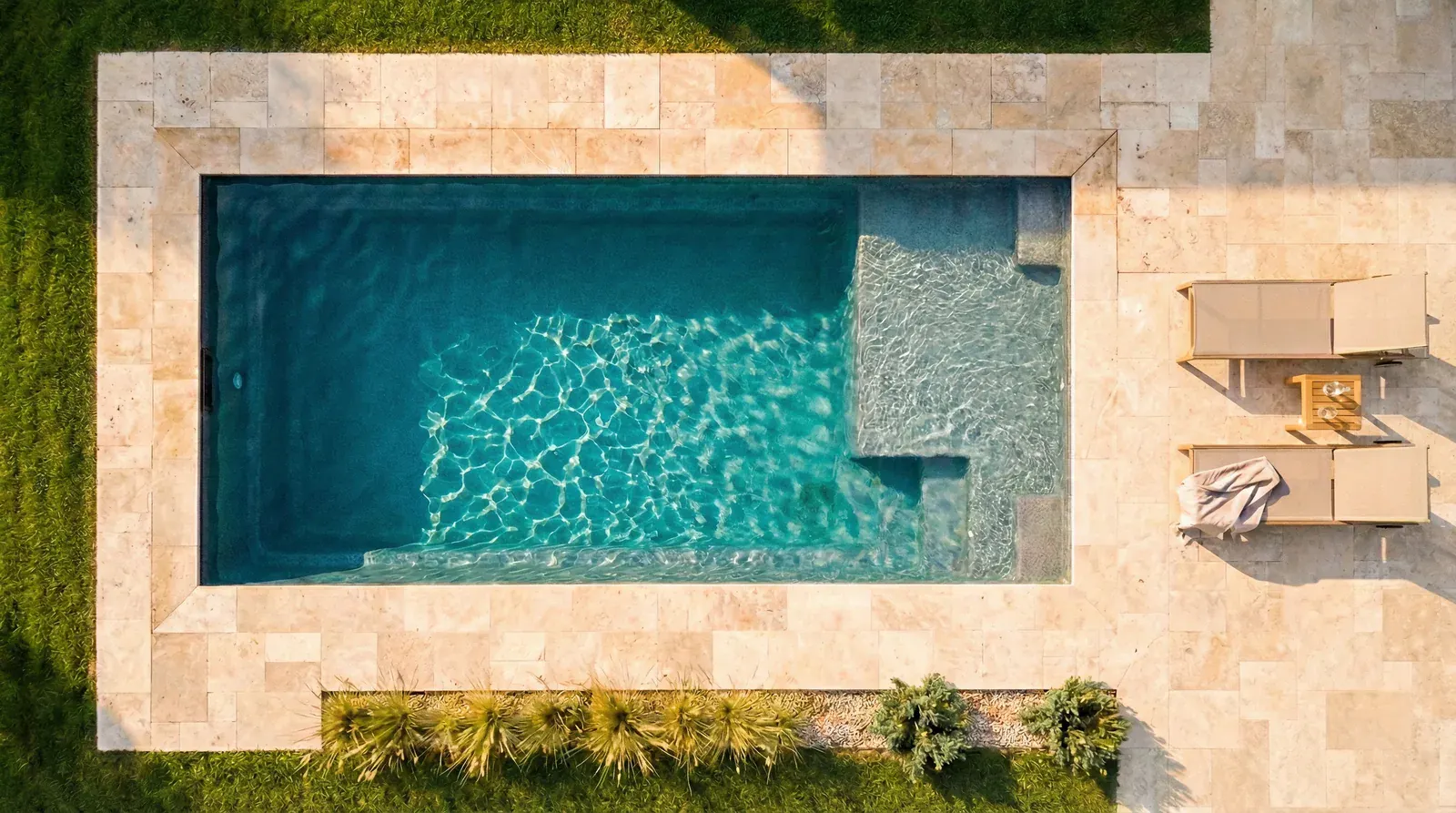 Vue aérienne d'une piscine coque avec plage immergée, margelles en travertin et transats teck