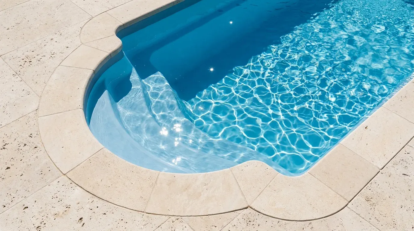 Détail d'une piscine coque type romaine avec escalier d'angle arrondi et margelle en pierre claire