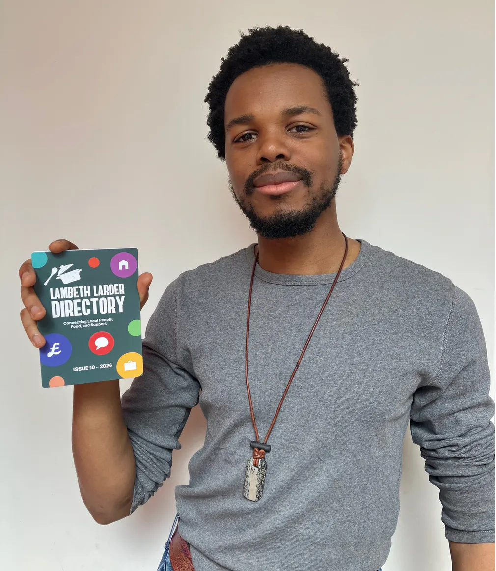 Young Black man wearing grey t-shirt, holding copy of Lambeth Larder directory