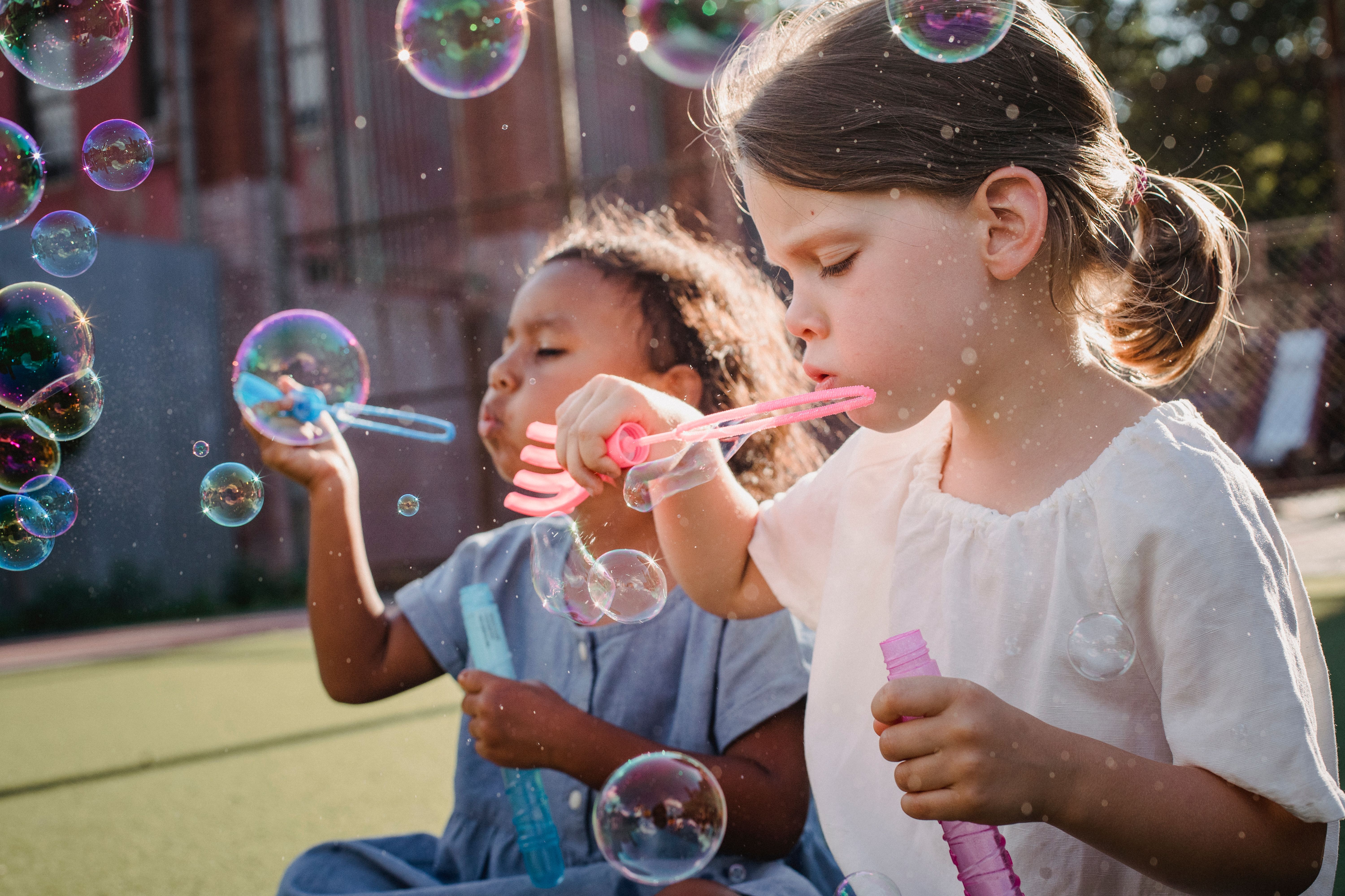 Two young girls blowing bubbles outside in sunshine.
