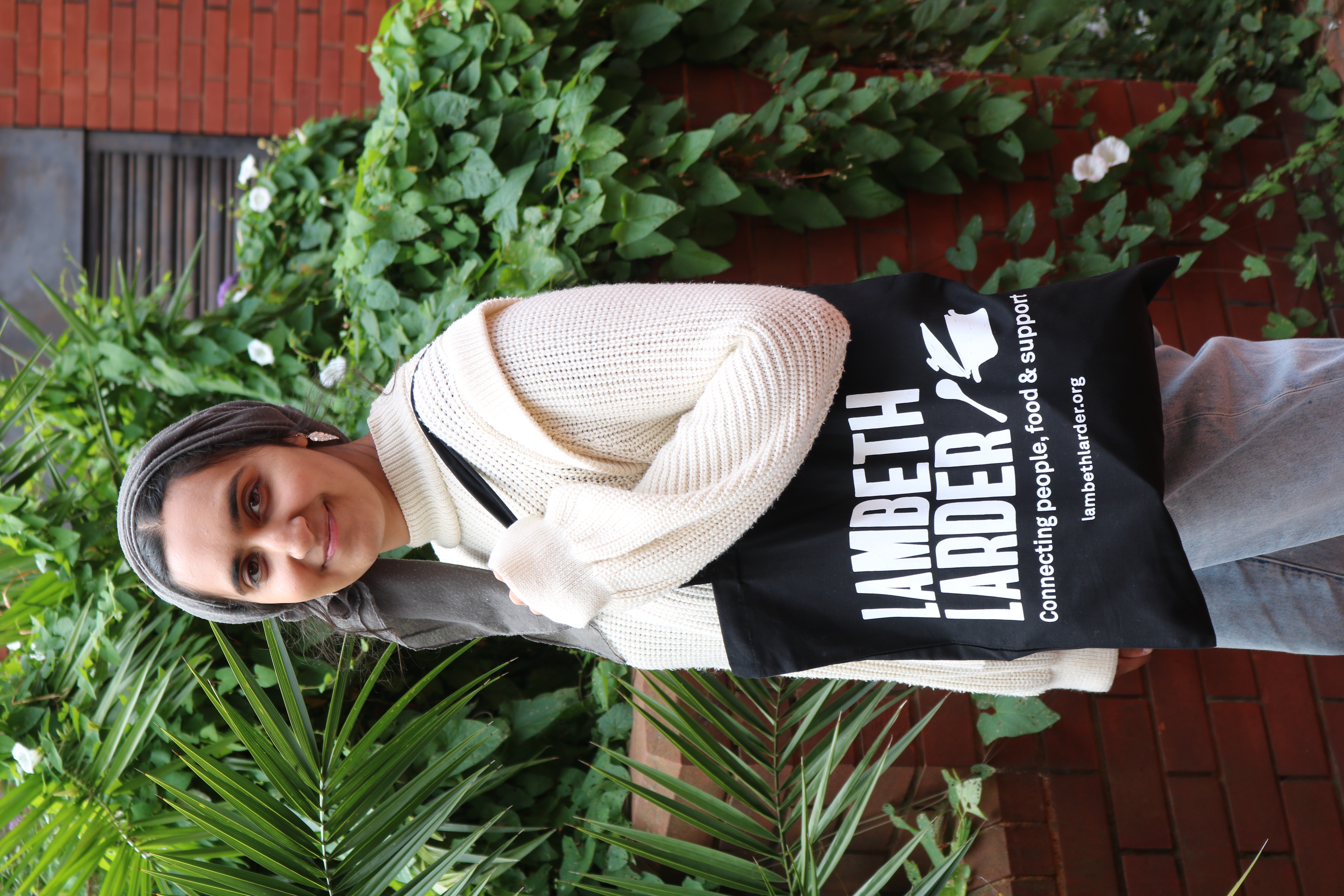 Young woman holding a black tote bag with white lettering that reads Lambeth Larder connecting people, food and support