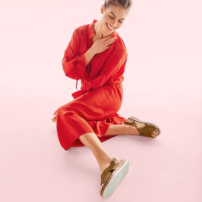 Model in sommerlichem, roten Jumpsuit mit Sandalen für anspruchsvolle Füße und Hallux valgus