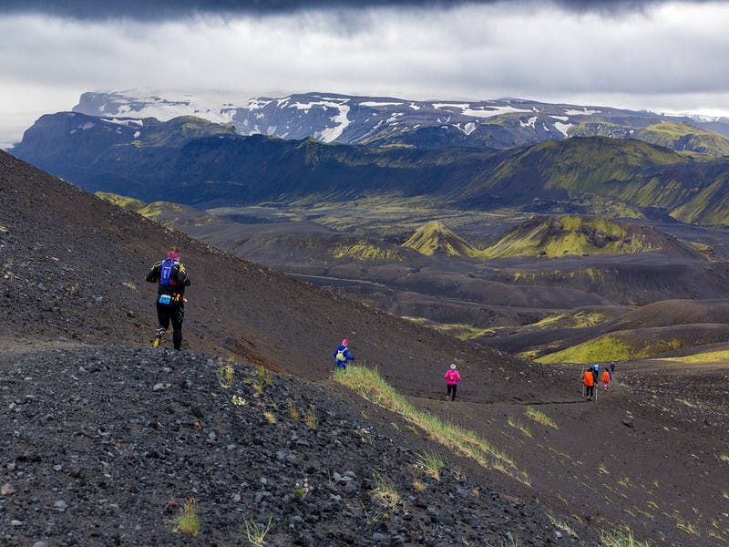 Þátttakendur á hlaupum í svörtum sandi með útsýni yfir falleg fjöll