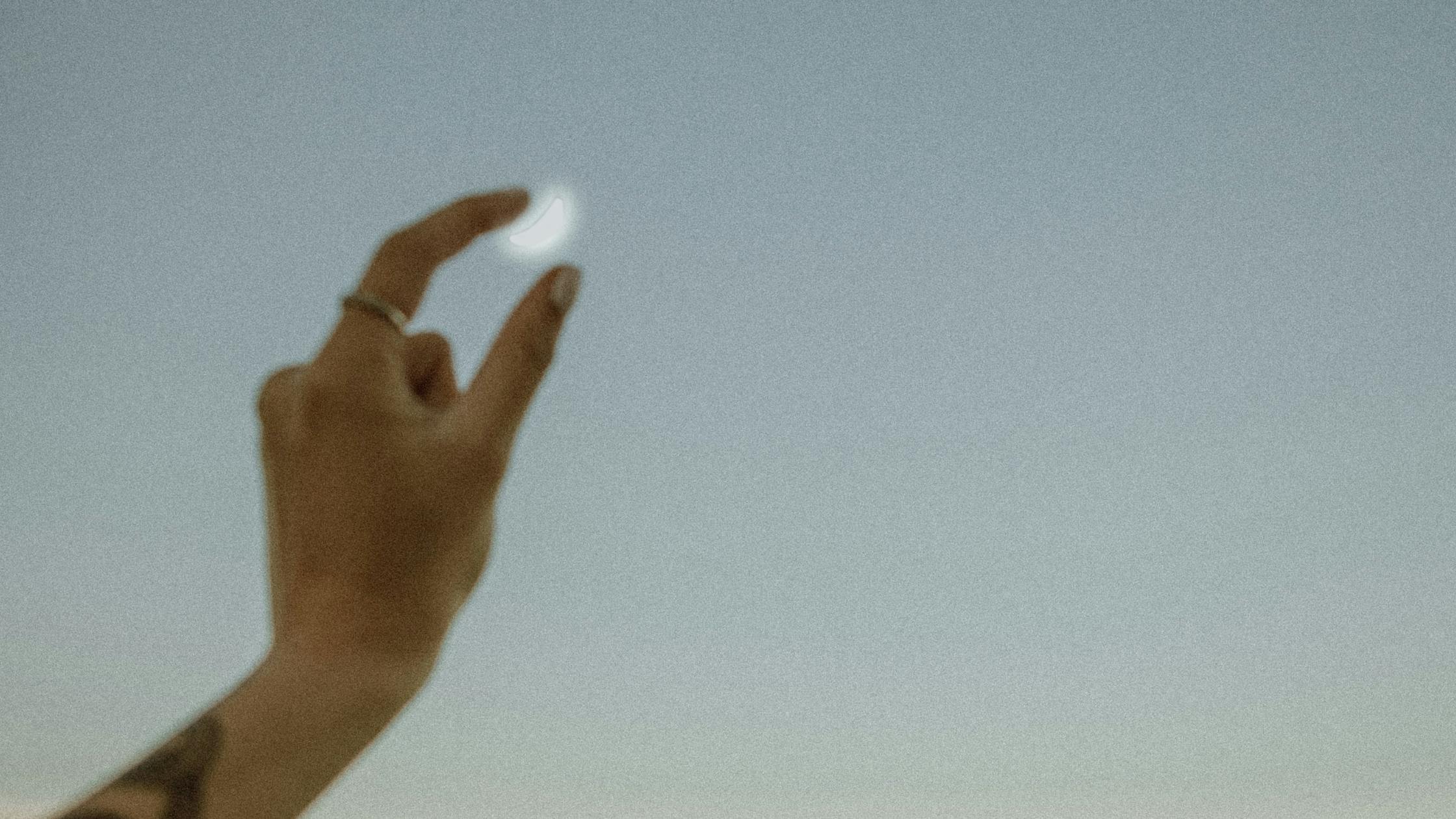 person's hand held up to the night sky, fingers pinching the moon