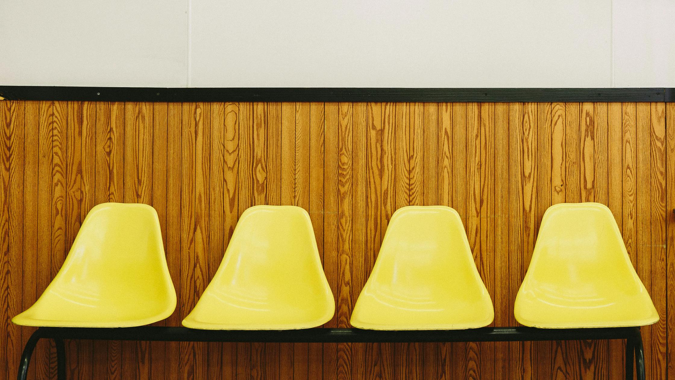 set of four yellow chairs in a row in an empty waiting room