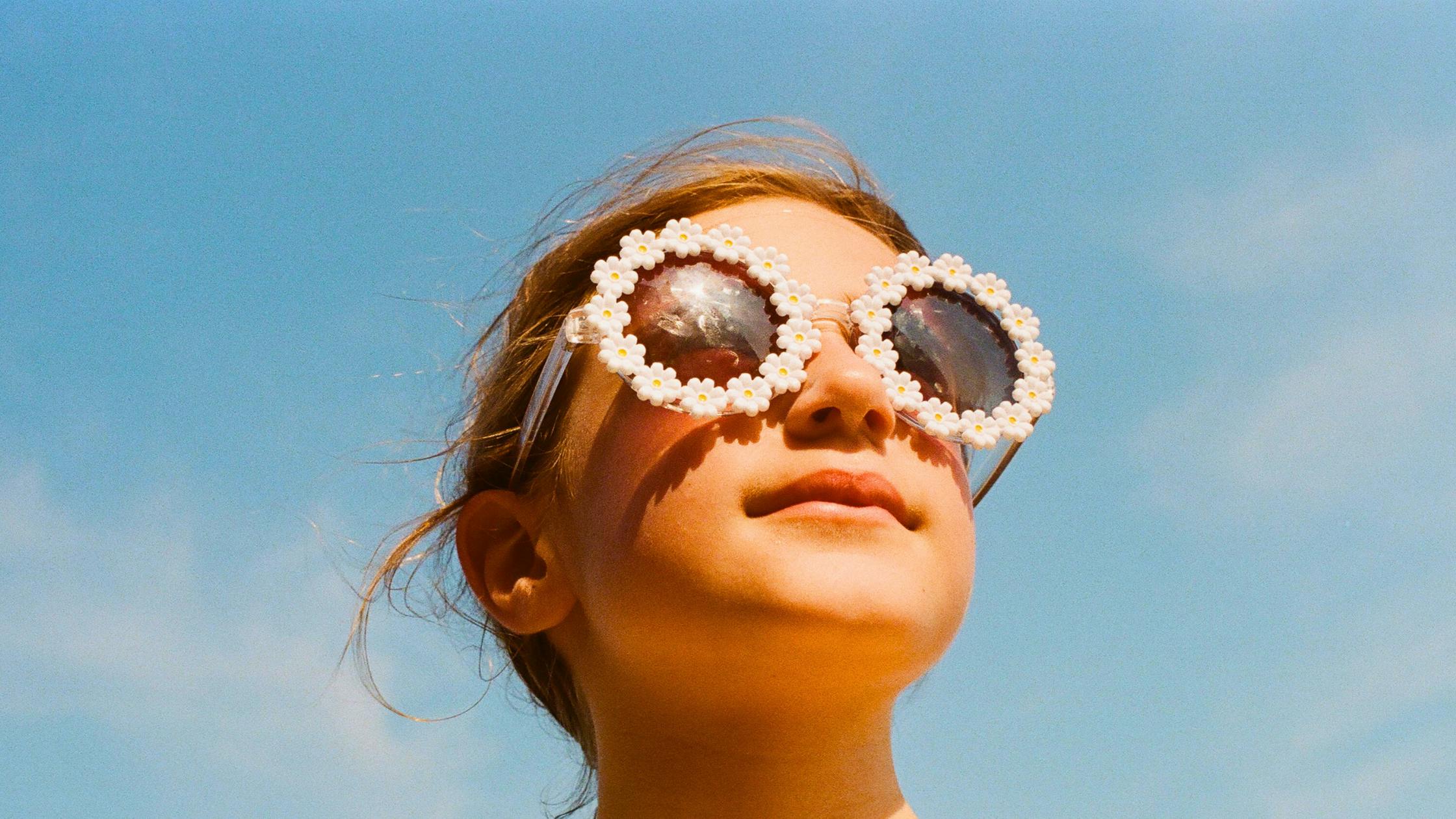 a little girl wearing flower sunglasses set against blue sky