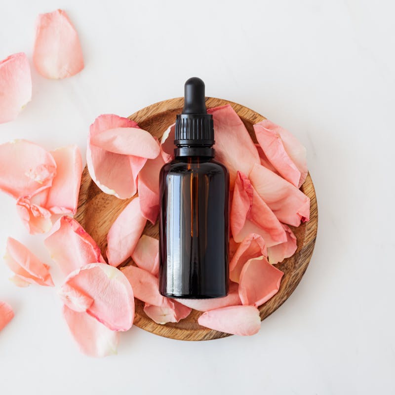 Essential oil bottle in the middle of a bowl with flower petals in it