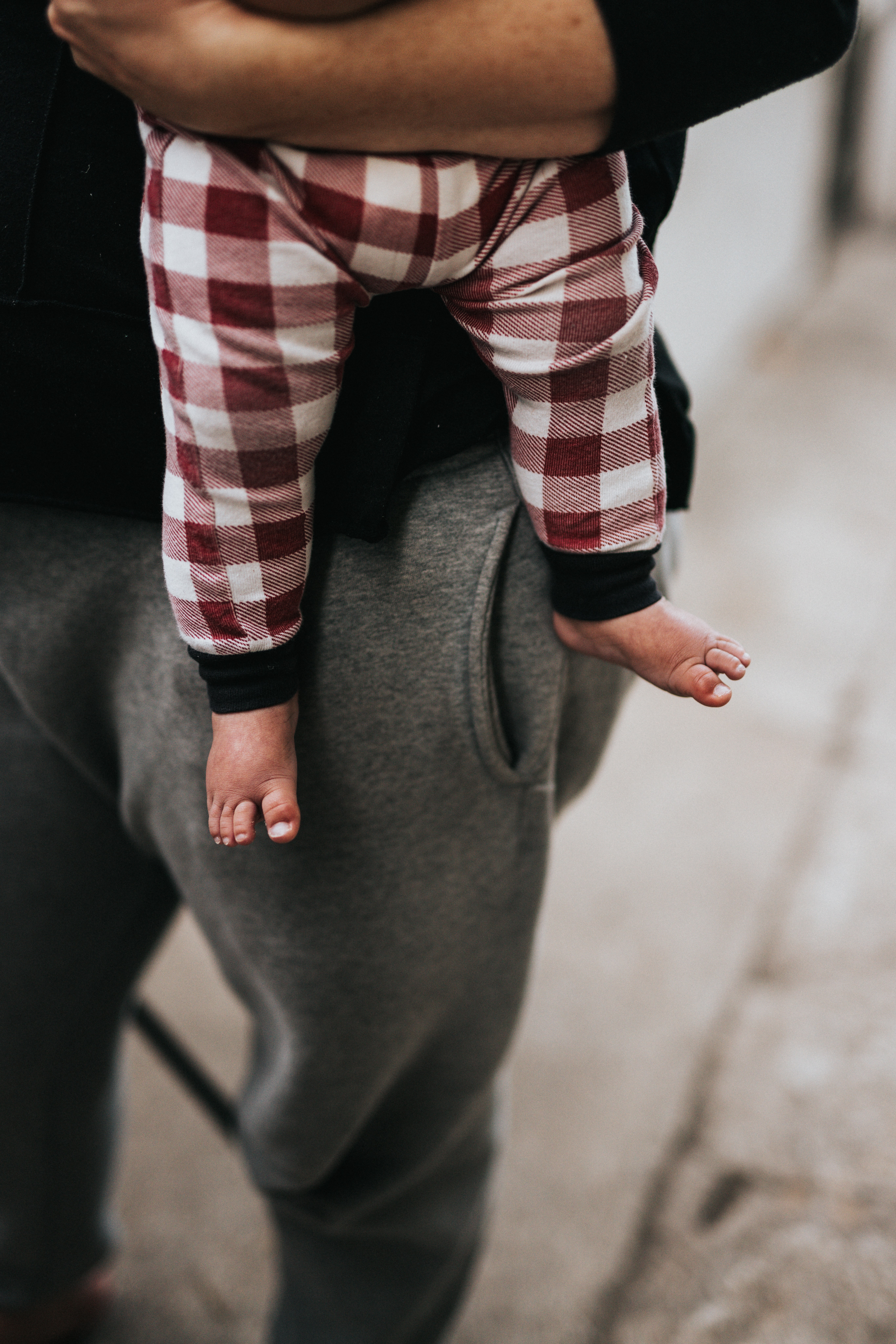 Baby with checkered pants being held by a parent.