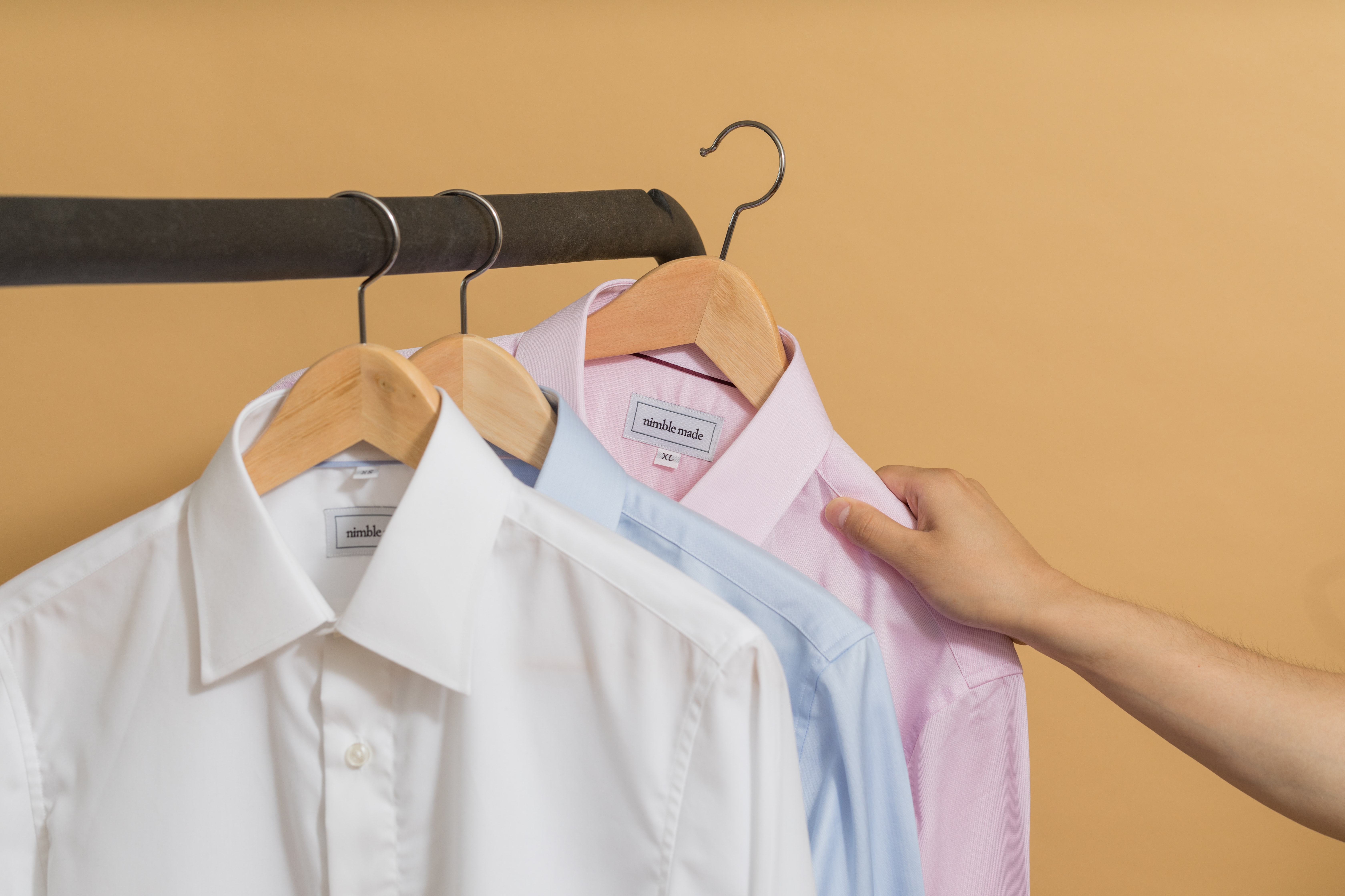 White and blue dress shirts hanging on a rack with a hand moving to