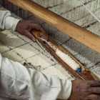 Weaver’s hands guiding a wooden shuttle across a loom, creating a thick wool rug.
