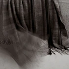 Dark textured shawl in motion, with soft folds and fringe against a light background.