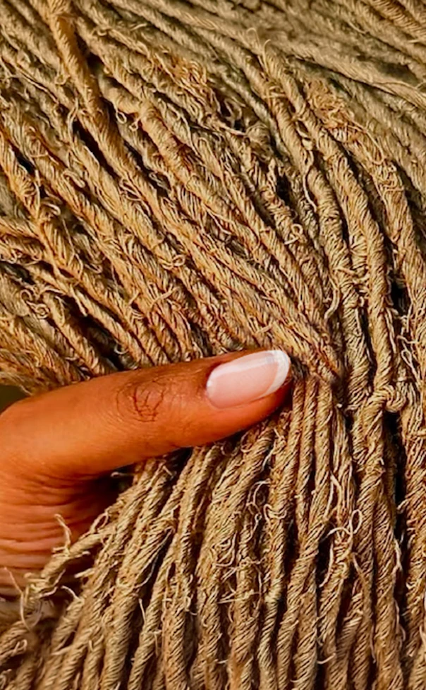 Hand holding a dense bundle of coarse tan twine or jute strands.