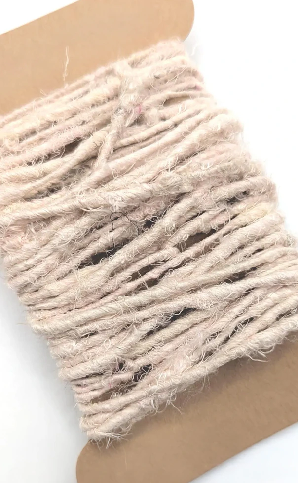 Flat cardboard bobbin wrapped with thick, fuzzy off white yarn on a white background.