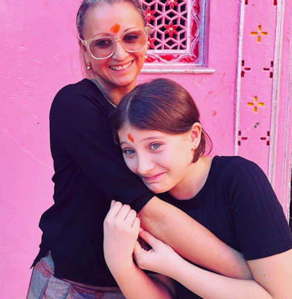 Mariella Ienna and with her daughter smiling and embracing in front of a bright pink wall.