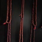 Three long rudraksha bead necklaces with red tassels hanging against a black background.
