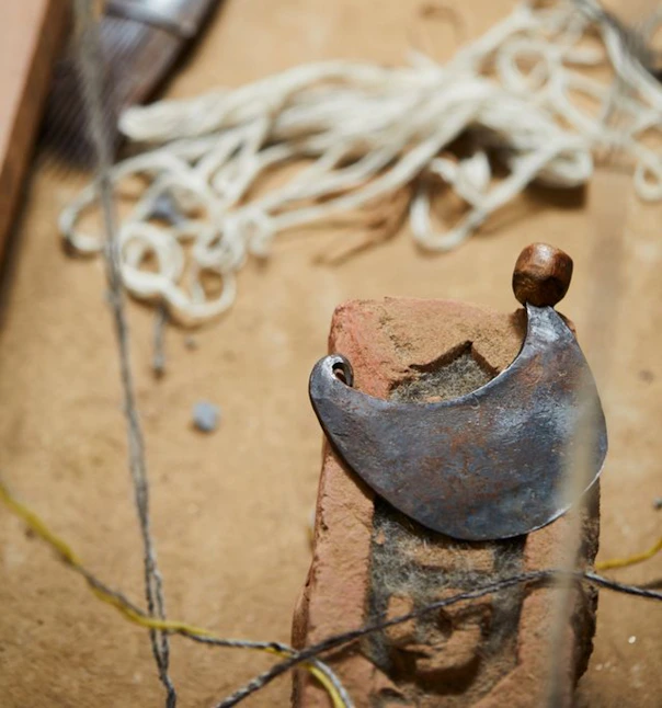 Forged crescent shaped metal piece resting on a rough brick amid string and workshop debris.