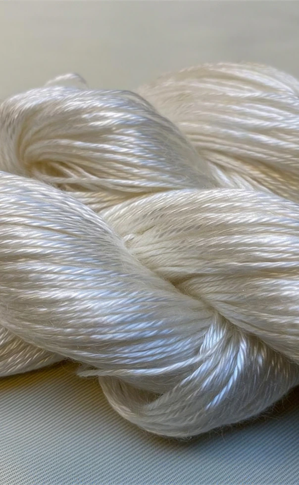 Close-up of glossy off white yarn twisted into thick, silky skeins on a neutral background.