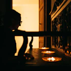 Silhouette of a person looking at three small candles glowing on a low wooden surface.