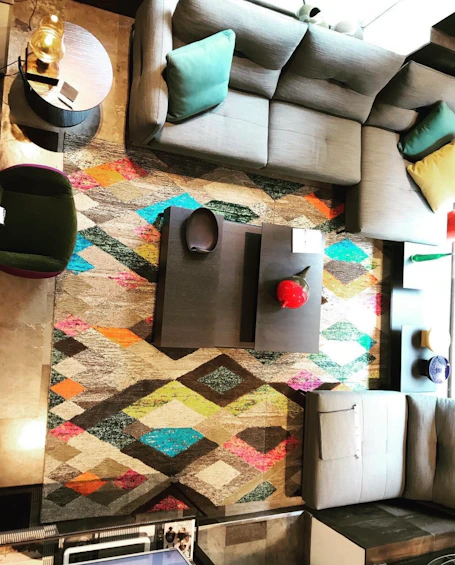 Top-down view of a grey sectional sofa around a colorful geometric rug with a low black coffee table.