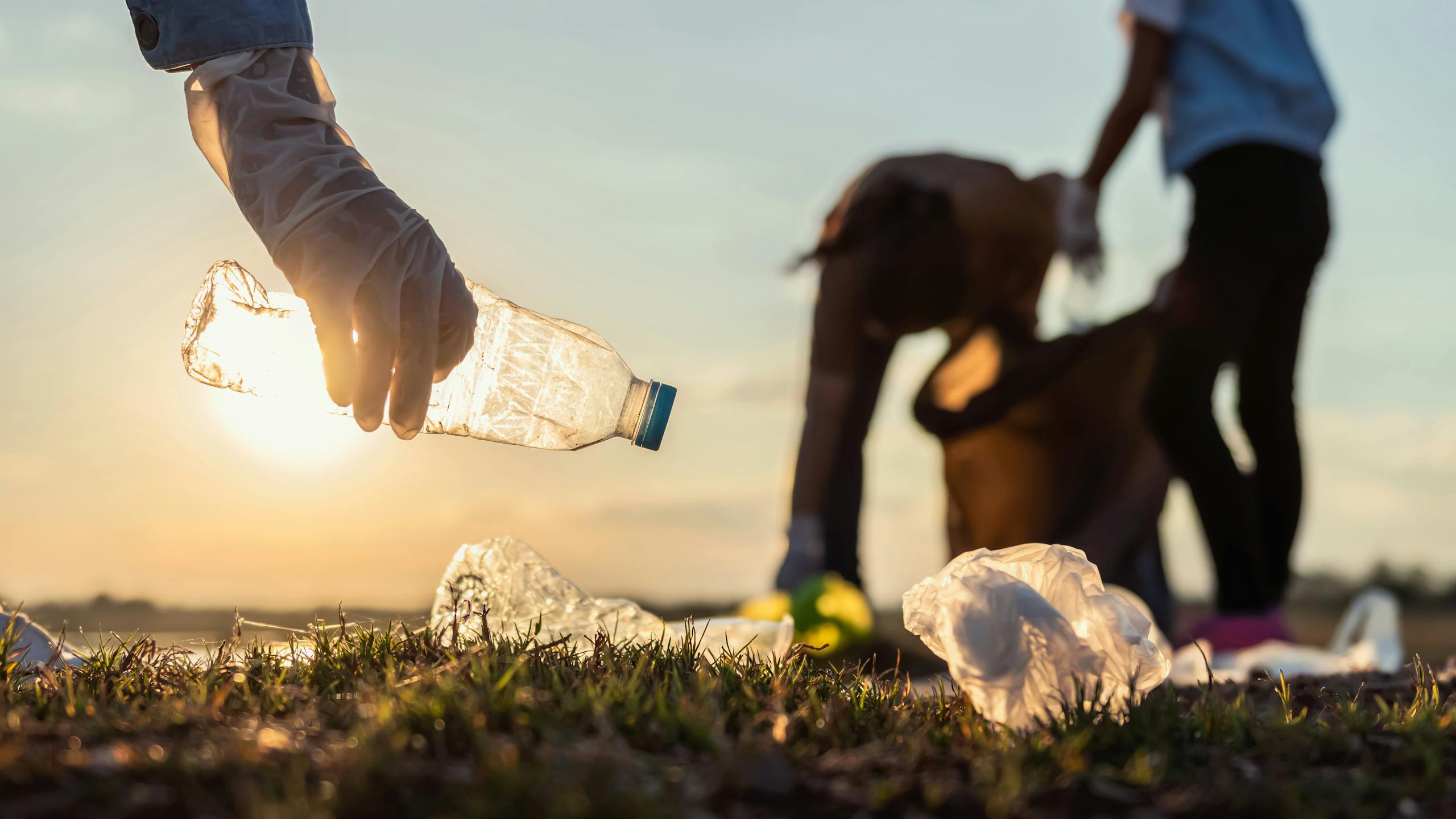 Image de quelqu'un avec un gant qui ramasse une bouteille d'eau. Dans le fond plusieurs personnes faisant la même chose.