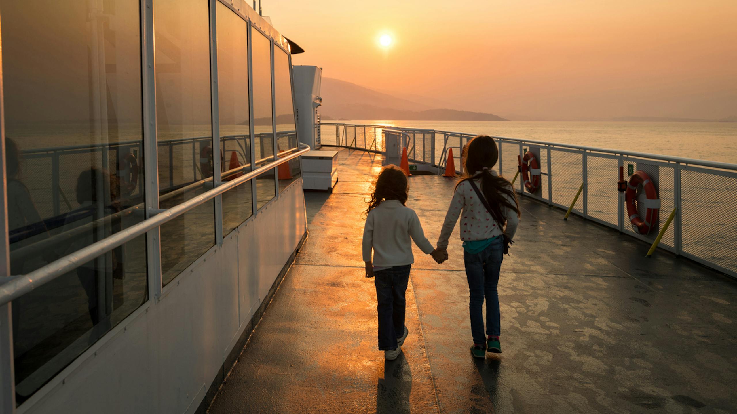 Enfants se tenant la main sur un ferry au coucher du soleil
