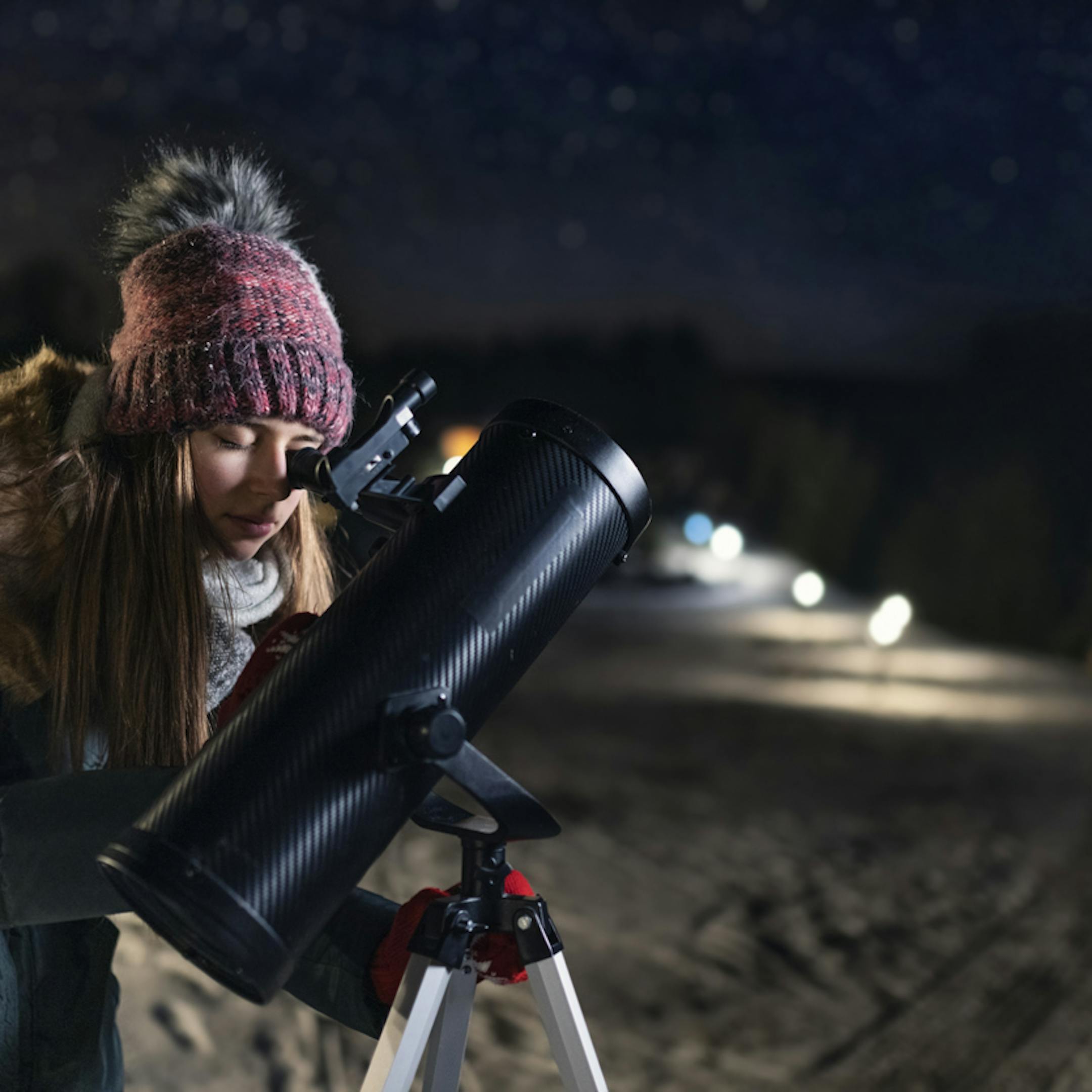 Jeune femme observant le ciel à l'aide d'un téléscope de nuit