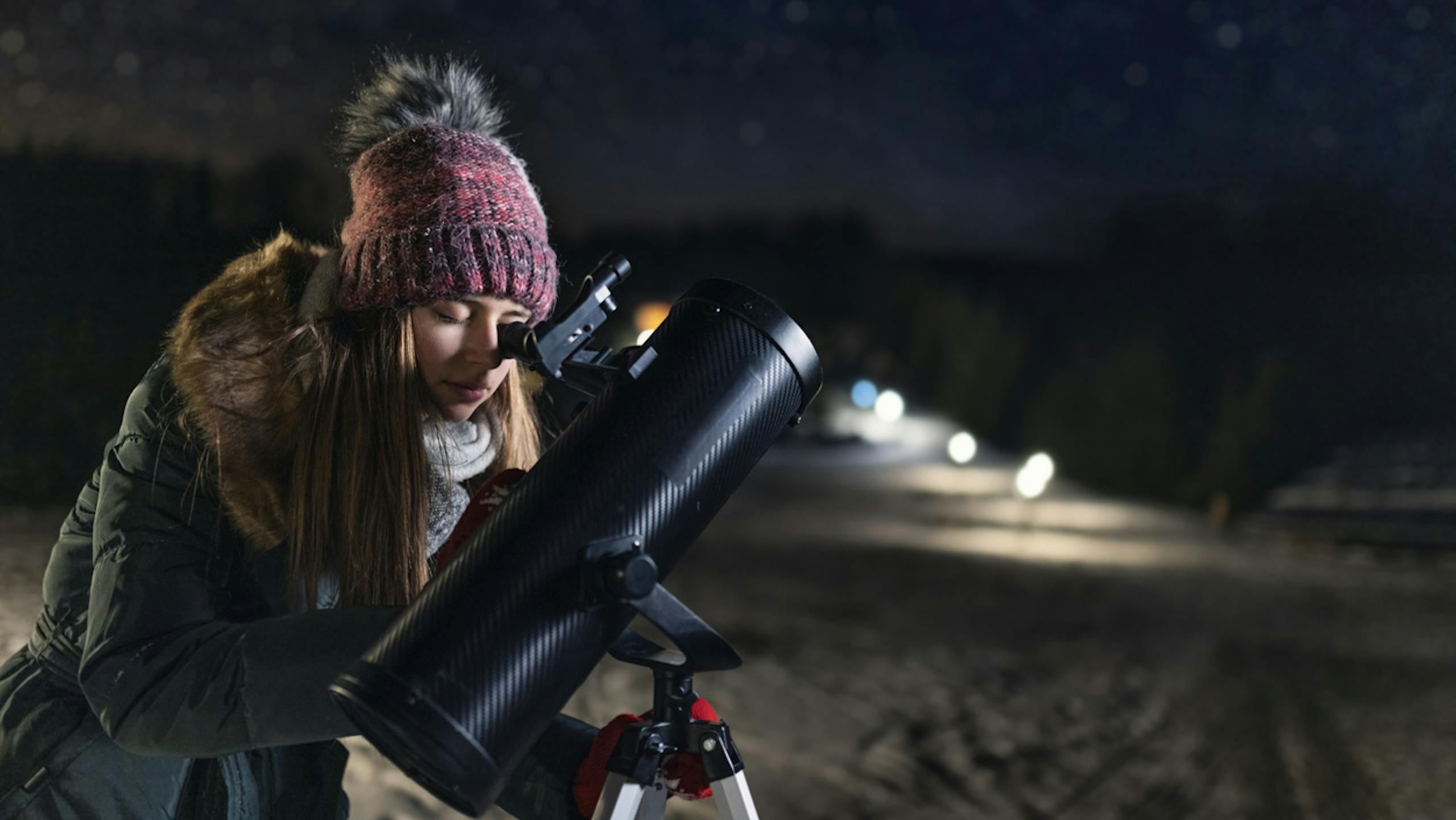 Jeune femme observant le ciel à l'aide d'un téléscope de nuit