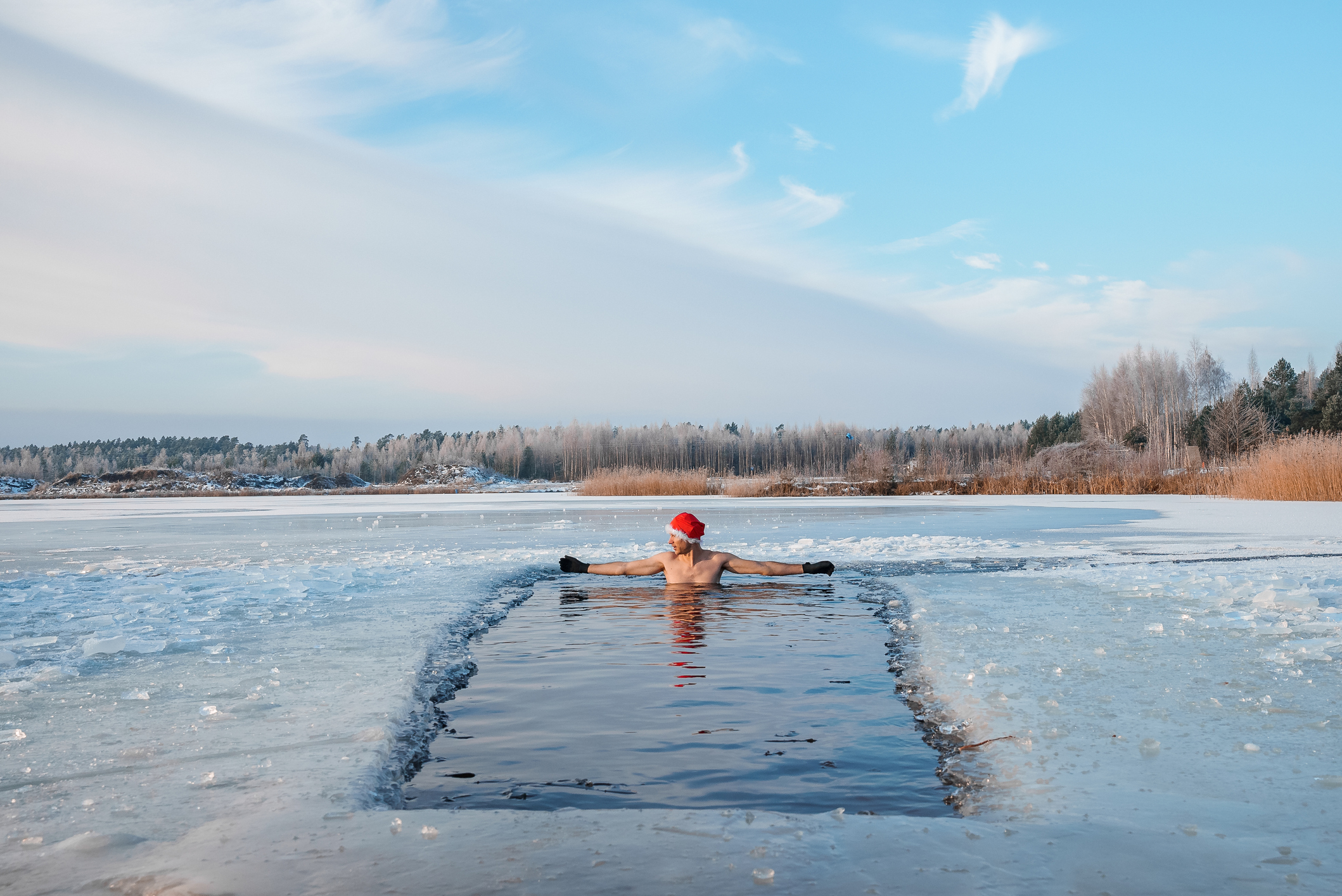 Homme coiffé d'un bonnet de Père Noël se baignant dans un lac glacé