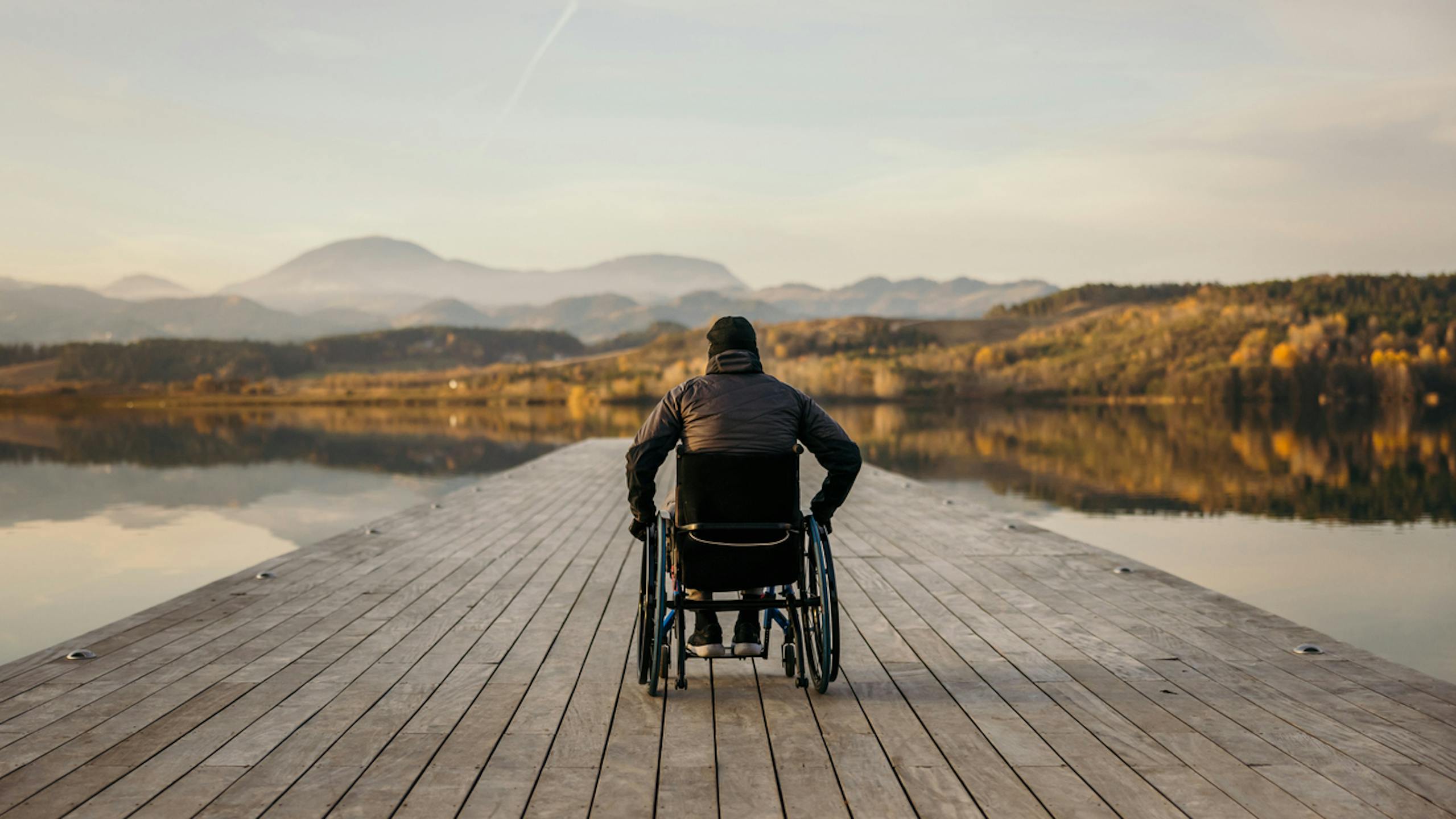 Homme handicapé assis en fauteuil roulant sur la jetée et admirant la nature au bord du lac